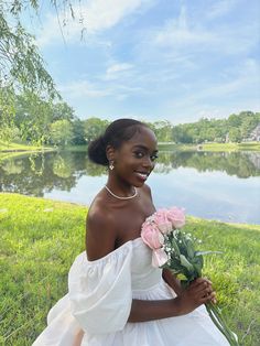 a woman in a white dress holding flowers near the water and smiling at the camera