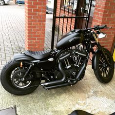 a black motorcycle parked next to a brick wall near a metal gate and fenced in area