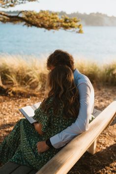 a man and woman sitting on a bench next to each other looking at the water