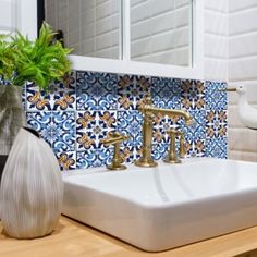 a white sink sitting under a bathroom mirror next to a vase with a green plant