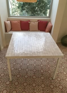 a white table sitting in front of a window next to a red and pink pillow