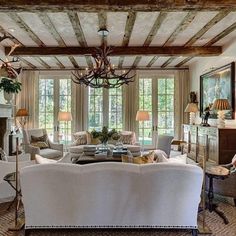 a living room filled with furniture and a chandelier hanging from the ceiling in front of two windows