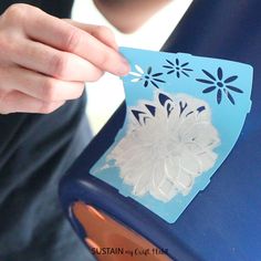 a person holding a piece of paper with flowers cut out of it on top of a blue chair