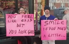 two people holding up pink signs in front of a store window that says, you feel like crap but if you need a little