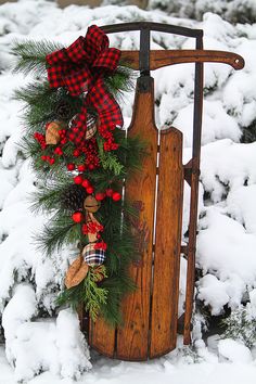 a sled decorated with pine, red and black plaid christmas wreath sits in the snow