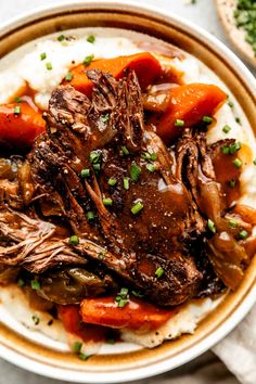 a bowl filled with meat, carrots and mashed potatoes on top of a table