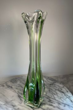 a green glass vase sitting on top of a marble table next to a white wall