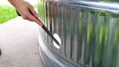 a person holding a knife near a large metal trash can with grass in the background