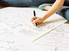 a woman is writing on a large sheet of paper with handwritten letters and numbers