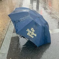 a blue umbrella sitting on the side of a wet street next to a sidewalk with people holding umbrellas