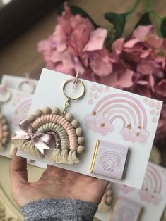 a hand holding a keychain that has some beads on it and a pink flower in the background