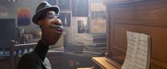 a man wearing glasses and a hat next to a piano with sheet music on it