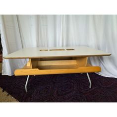 a wooden table with metal legs and an open laptop on it's top, in front of a white curtain