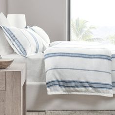 a bed with white and blue striped linens next to a window in a bedroom