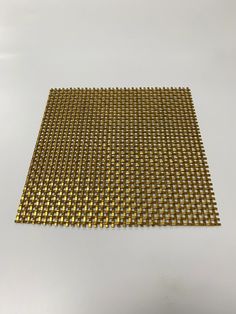 a piece of gold colored metal mesh on a white surface with small holes in the middle