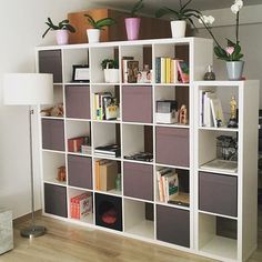 a white book shelf filled with books next to a lamp and vases on top of it