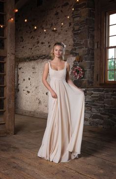 a woman in a white dress standing on a wooden floor next to a brick wall