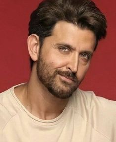 a close up of a person wearing a white shirt and beard with a red wall in the background