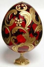 an ornate red and gold decorated egg on a golden stand, with white back ground