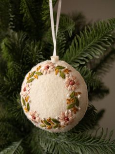 an ornament hanging from a christmas tree with leaves and flowers on it's side