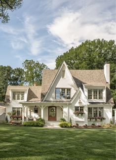 a large white house with lots of windows and plants on the front lawn, surrounded by lush green grass