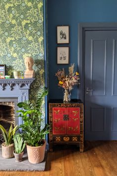 a living room with blue walls and wooden floors, two potted plants in front of the fireplace