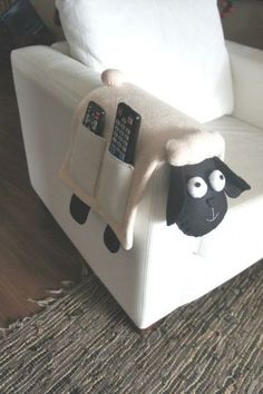 a stuffed sheep sitting on top of a white chair next to a pillow and remote control