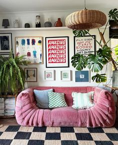 a living room filled with lots of plants and pictures hanging on the wall next to a pink couch