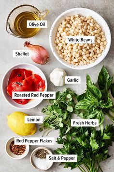 ingredients to make white bean salad laid out in bowls on a gray surface with lemons, pepper, garlic, and parsley