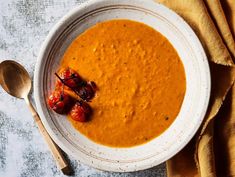 a white bowl filled with carrot soup and garnished with crumbled tomatoes