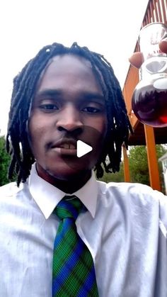 a man with dreadlocks wearing a green tie and drinking from a glass in front of him