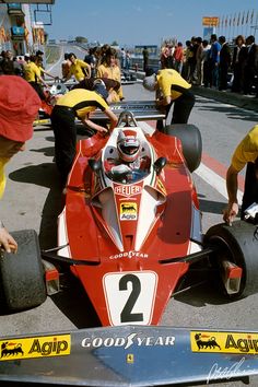 a man in a race car with other people around him looking at the front wheel