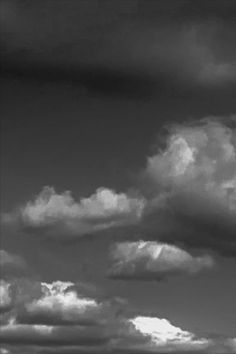 a black and white photo of clouds in the sky above a field with cows grazing on it