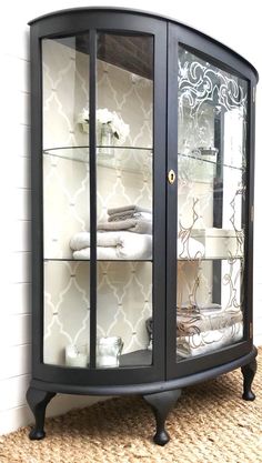 a black corner cabinet with glass doors on the top and shelves below it that have folded towels in them