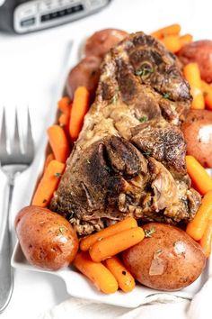 a white plate topped with meat and carrots next to potatoes on top of a table