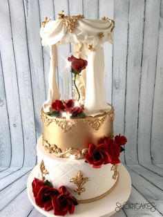 a three tiered wedding cake with red roses on the bottom and gold trimmings