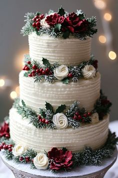 a three tiered cake decorated with holly and red flowers on a platter in front of christmas lights