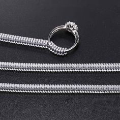 a pair of silver colored metal zippers on a black surface with a diamond ring in the middle