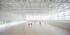 an indoor basketball court with people playing on the floor and in the background are large windows