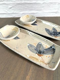 two serving dishes with leaves on them sitting on a table