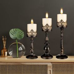 three candles sitting on top of a wooden table next to a vase with a green plant