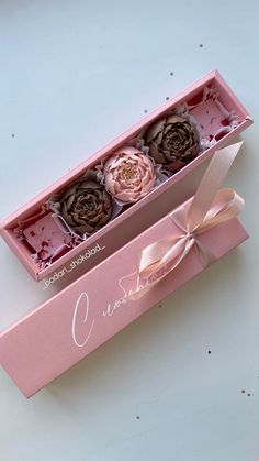 three roses in a pink box with ribbon on the bottom and one flower inside it