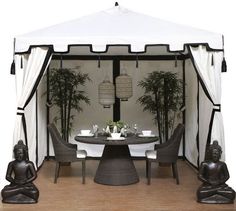 a white tent with buddha statues in front of it on a wooden floor next to a table and chairs