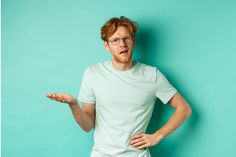 a man with glasses is holding his hand up in the air while standing against a turquoise background