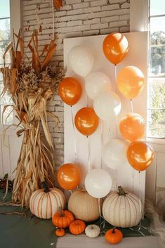 balloons and pumpkins are arranged on the floor in front of a brick wall with an arrangement of corn stalks