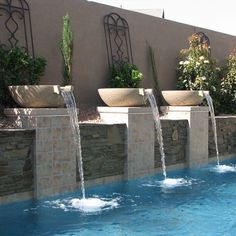 an outdoor swimming pool with water running from the sides and planters on each side