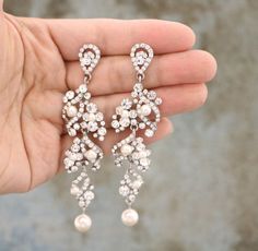 a pair of white pearl and crystal chandelier earrings on a person's hand