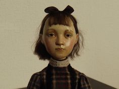 the doll is wearing a black and brown plaid shirt with a bow on her head