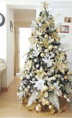 a white and gold christmas tree in a living room with ornaments on the top, silver and gold decorations on the bottom