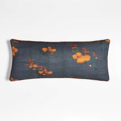 an orange and blue pillow with flowers on it, sitting on a white surface next to a wall